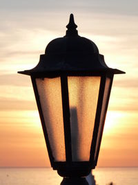 Close-up of silhouette built structure against sea at sunset
