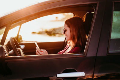 Woman sitting in car and using smartphone