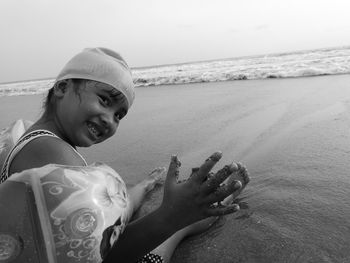 Portrait of happy girl sitting on shore at beach against clear sky