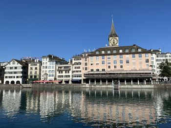 Buildings by river against clear blue sky