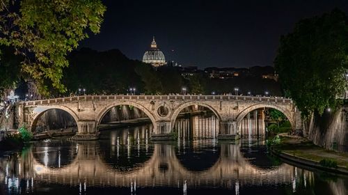 Arch bridge over river by buildings against sky at night