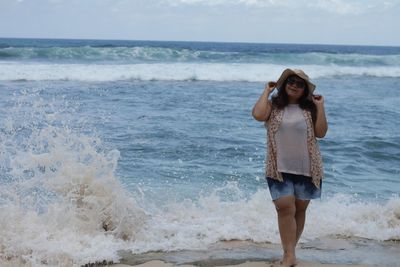 Young woman standing on beach against sky