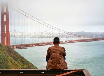 Rear view of man looking at suspension bridge against sky