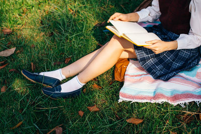 Low section of woman reading book on field