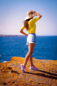 Side view of mid adult woman wearing hat standing at beach against sky during sunny day