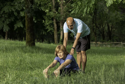 Senior couple, man helping woman gain flexibility while relaxing on the grass in nature enviroment
