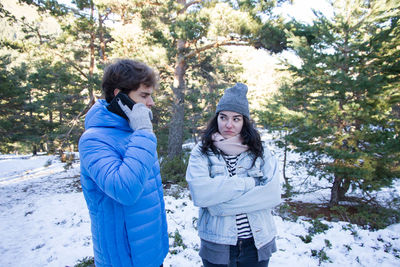 Man talking on mobile phone by angry woman while standing on snow covered field