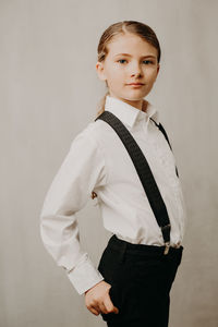 Portrait of girl wearing suspenders and shirt against white background