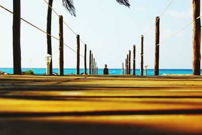 Surface level of boardwalk leading towards sea against sky on sunny day