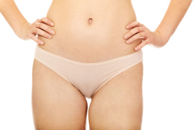 Midsection of young woman with hands on hip standing against white background