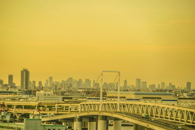 Bridge over buildings in city against sky during sunset