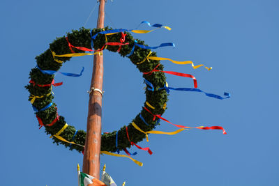 Low angle view of wreath with colorful ribbons hanging on pole against clear blue sky
