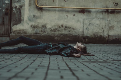 Side view of young woman sleeping on footpath