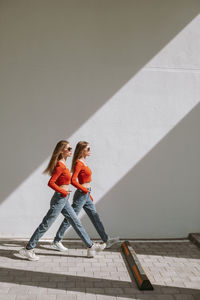 The twin sisters stepping forward in sync. diagonal shadow of natural sunlight, urban area.