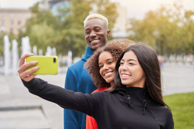 Smiling friends taking selfie while standing outdoors