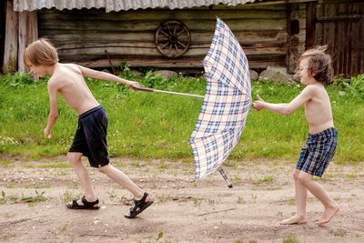 Side view of brothers holding umbrella while running on land