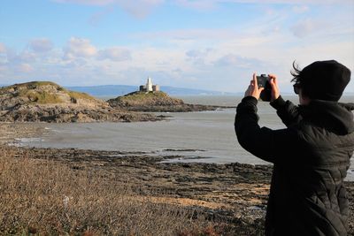 Rear view of man photographing against sky