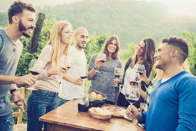 Smiling friends holding wineglass while standing around table