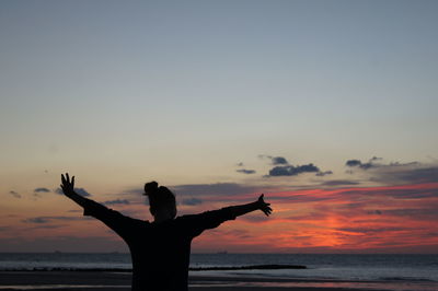 Silhouette woman standing on beach against sky during sunset