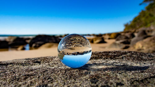 Close-up of crystal ball on beach against clear blue sky