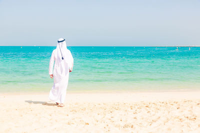 Rear view of man standing on beach against clear sky