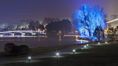 Illuminated city by river against sky at night