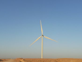 Windmill on field in desert against clear blue sky