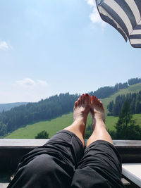 Low section of man relaxing on mountain against sky