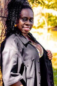 Portrait of smiling woman leaning on tree