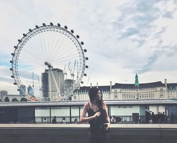 Woman standing by ferris wheel against sky