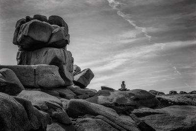 Low angle view of woman sitting on rock against sky