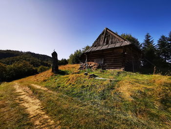 Abandoned wooden house on field by trees against sky