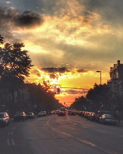Cars on road against cloudy sky during sunset