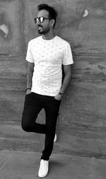 Full length of young man wearing sunglasses standing against wall
