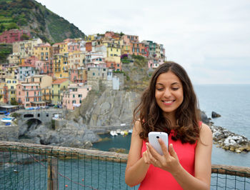 Beautiful young woman using smart phone by sea against sky
