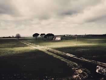 Road passing through field against cloudy sky
