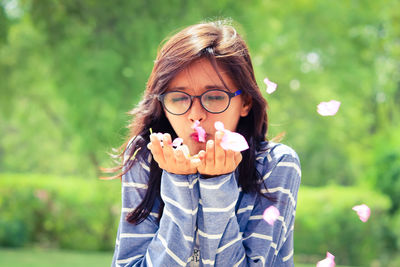 Young woman blowing flower petals at park