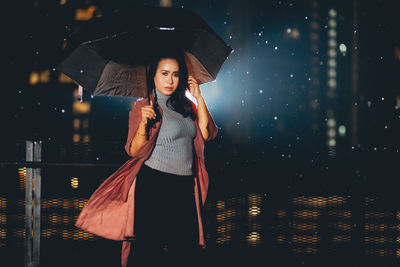 Woman standing with umbrella at night during rainy season