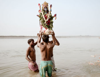 Full length of shirtless man standing in sea against sky