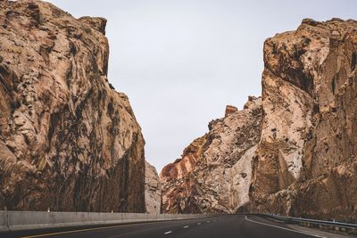 Empty road amidst rocky cliffs against sky