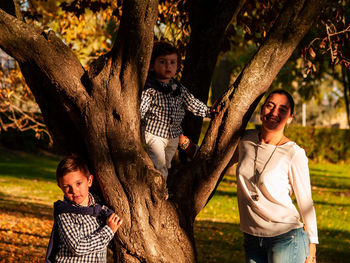 Portrait of mother and sons on tree trunk at park