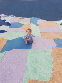 High angle view of cute boy sitting on painted map on walkway