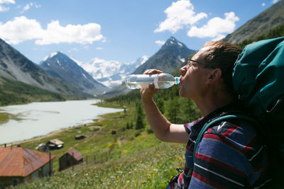 Backpacker drinking water while standing against mountains