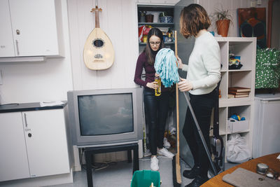 Young female roommates with cleaning equipment standing by closet in college dorm