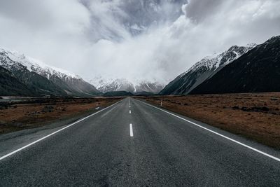 Empty road leading towards mountains against sky