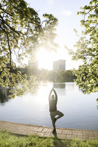 Man practicing yoga by lake in park