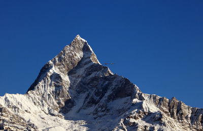 Low angle view of snowcapped mountain against clear blue sky