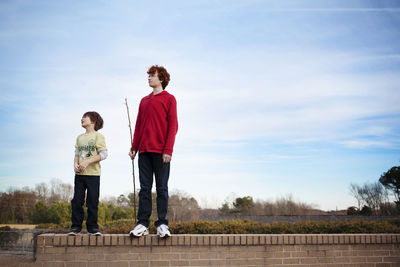 Brothers standing on retaining wall against sky