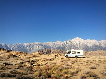 Travel trailer on field by rocky mountains against clear blue sky