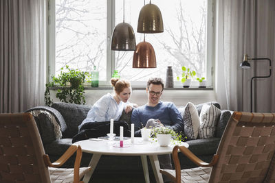 Couple looking in smartphone while sitting on sofa at home